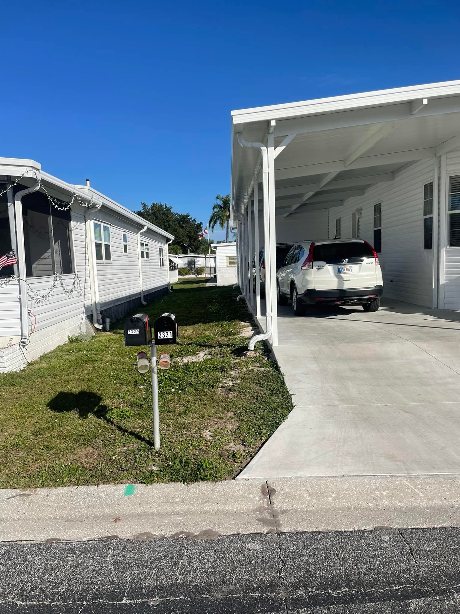 White mobile homes with carport and mailbox on a sunny day.