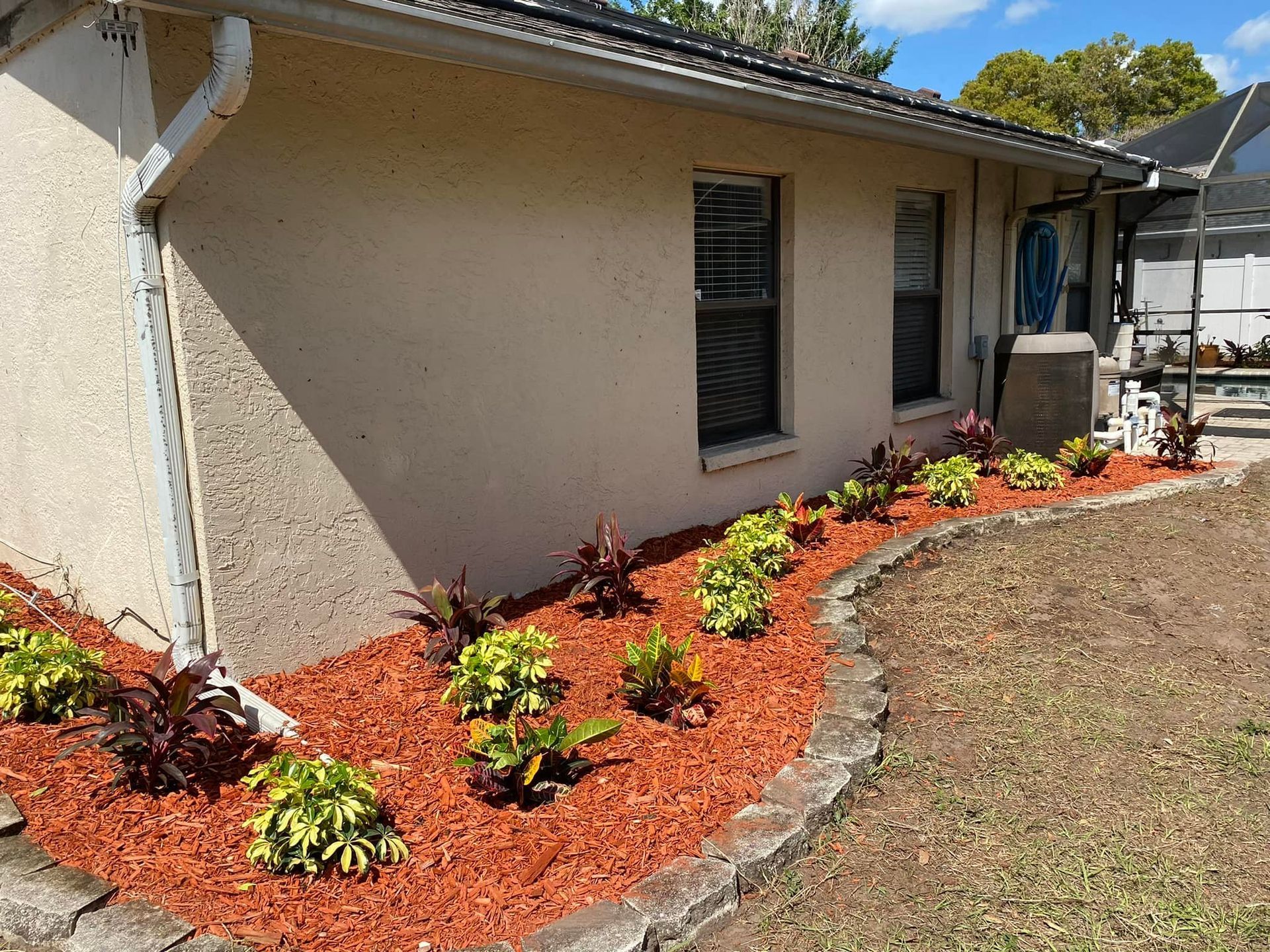 Beige house with a landscaped garden bed of red mulch and plants.