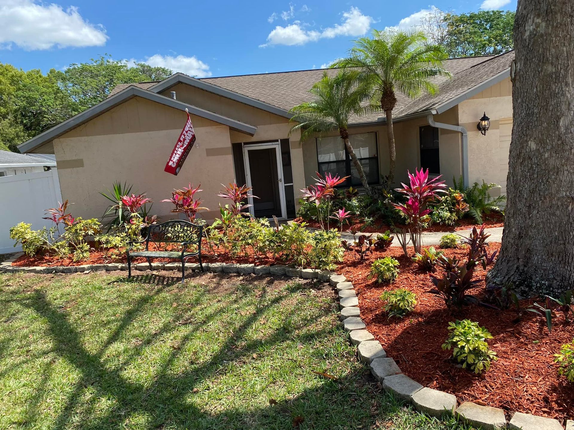 Tan house with red and green landscaping and a US flag.