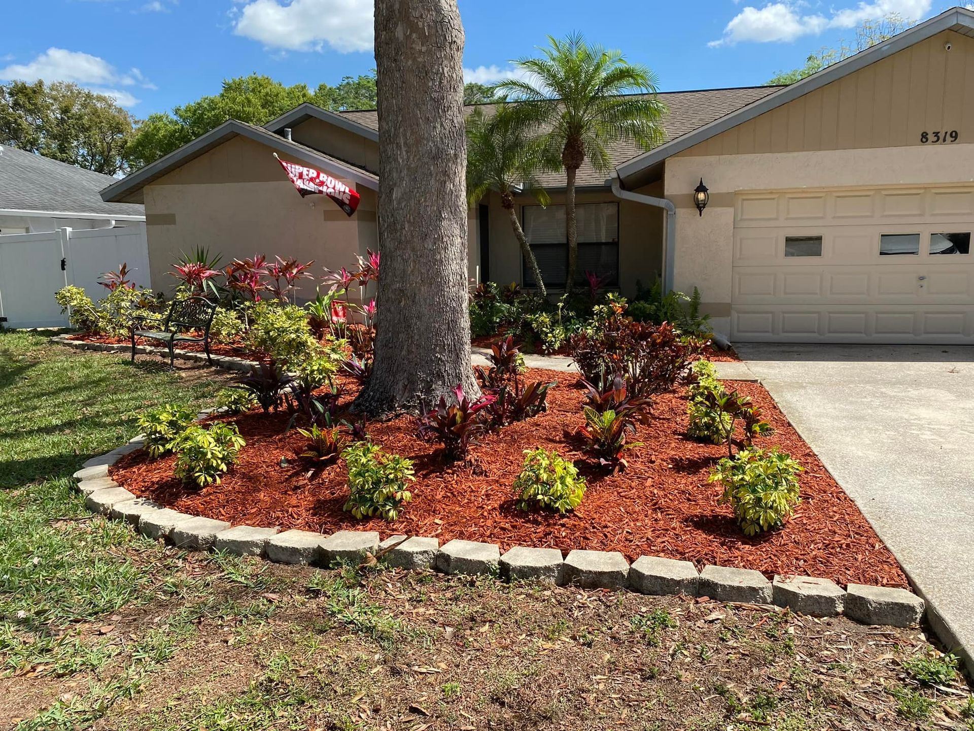 Front yard with mulch-covered flower bed, bordered by stone. Palm tree and house in the background.