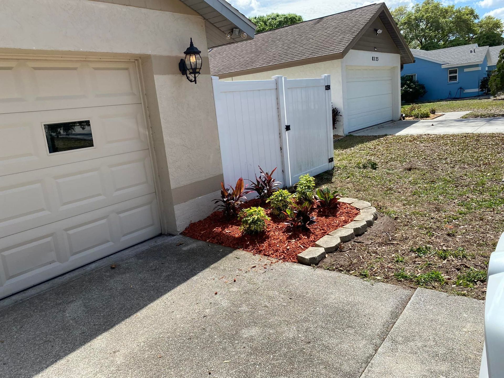 Garage and white fence with landscaped flower bed and red mulch.