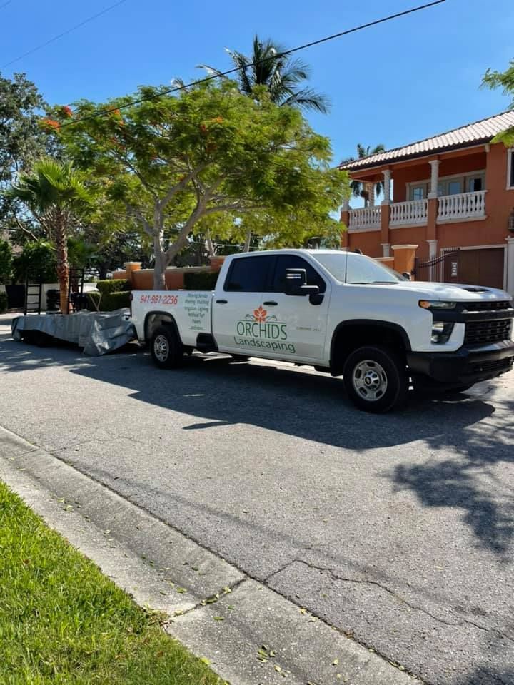White pickup truck with trailer on residential street, with landscaping business logo.