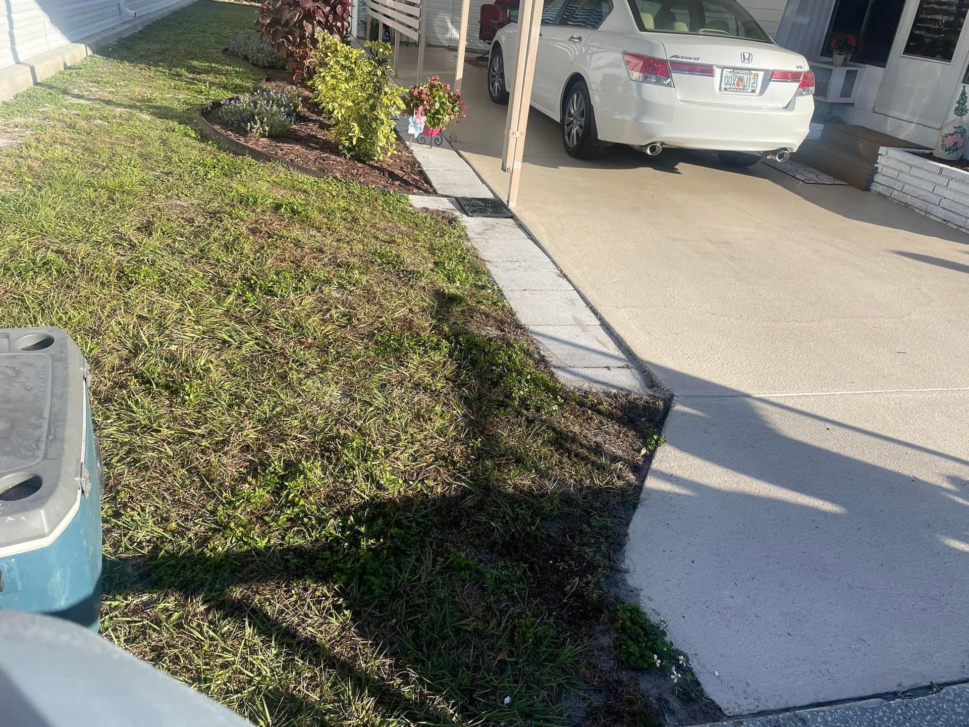 Grassy yard and concrete driveway; a white car is parked under a carport.
