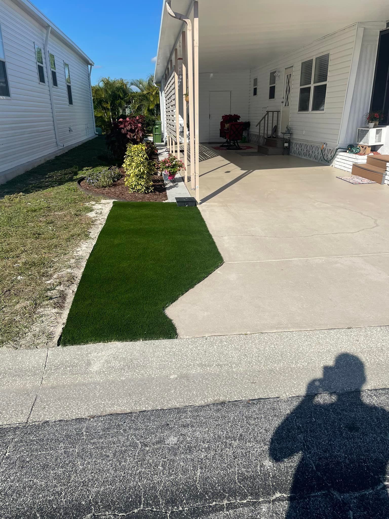 A walkway with artificial turf next to a mobile home, in a sunny setting.