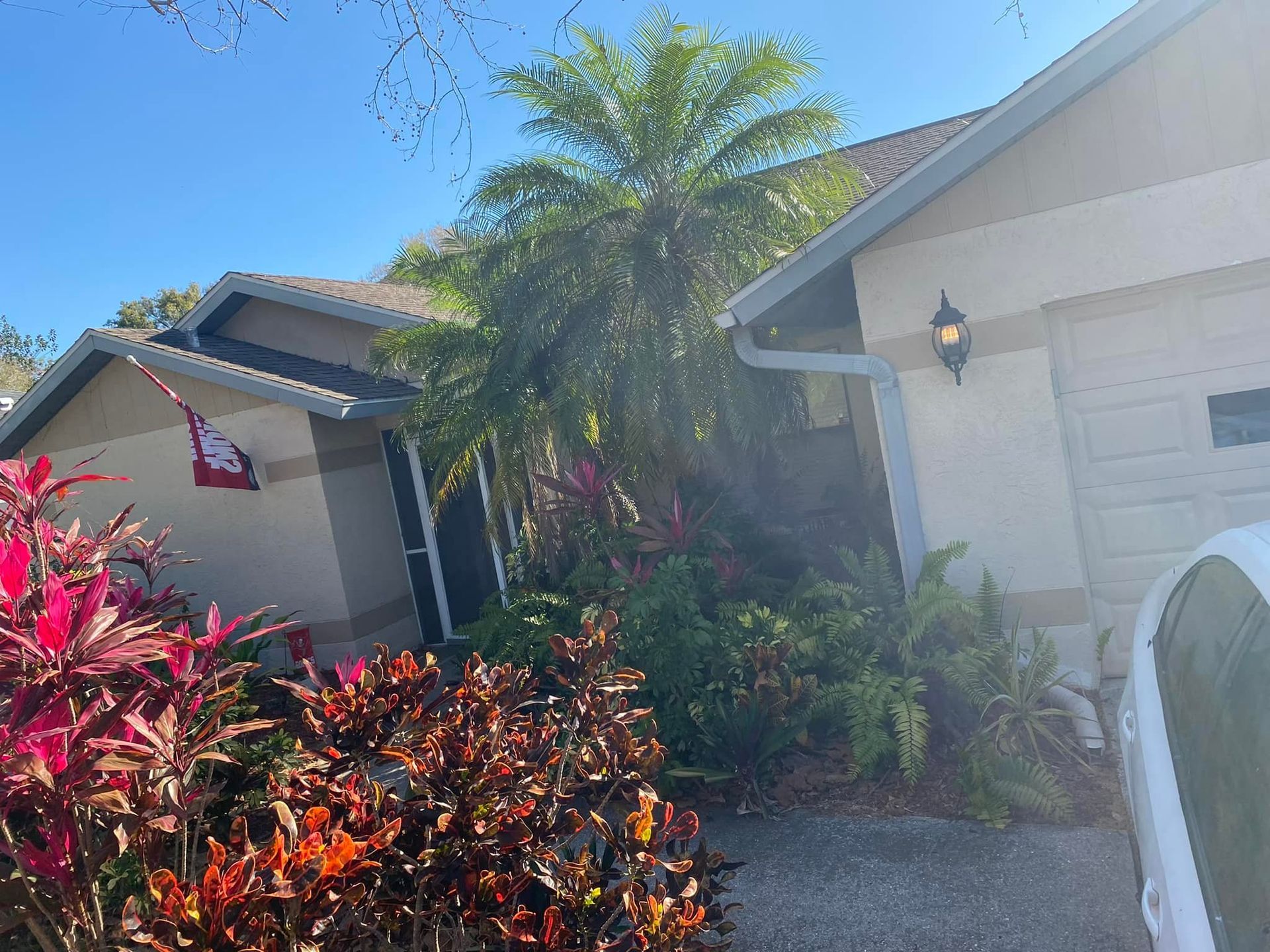 House exterior with tan siding, a garage, and tropical plants in front. A Hello Kitty flag hangs.