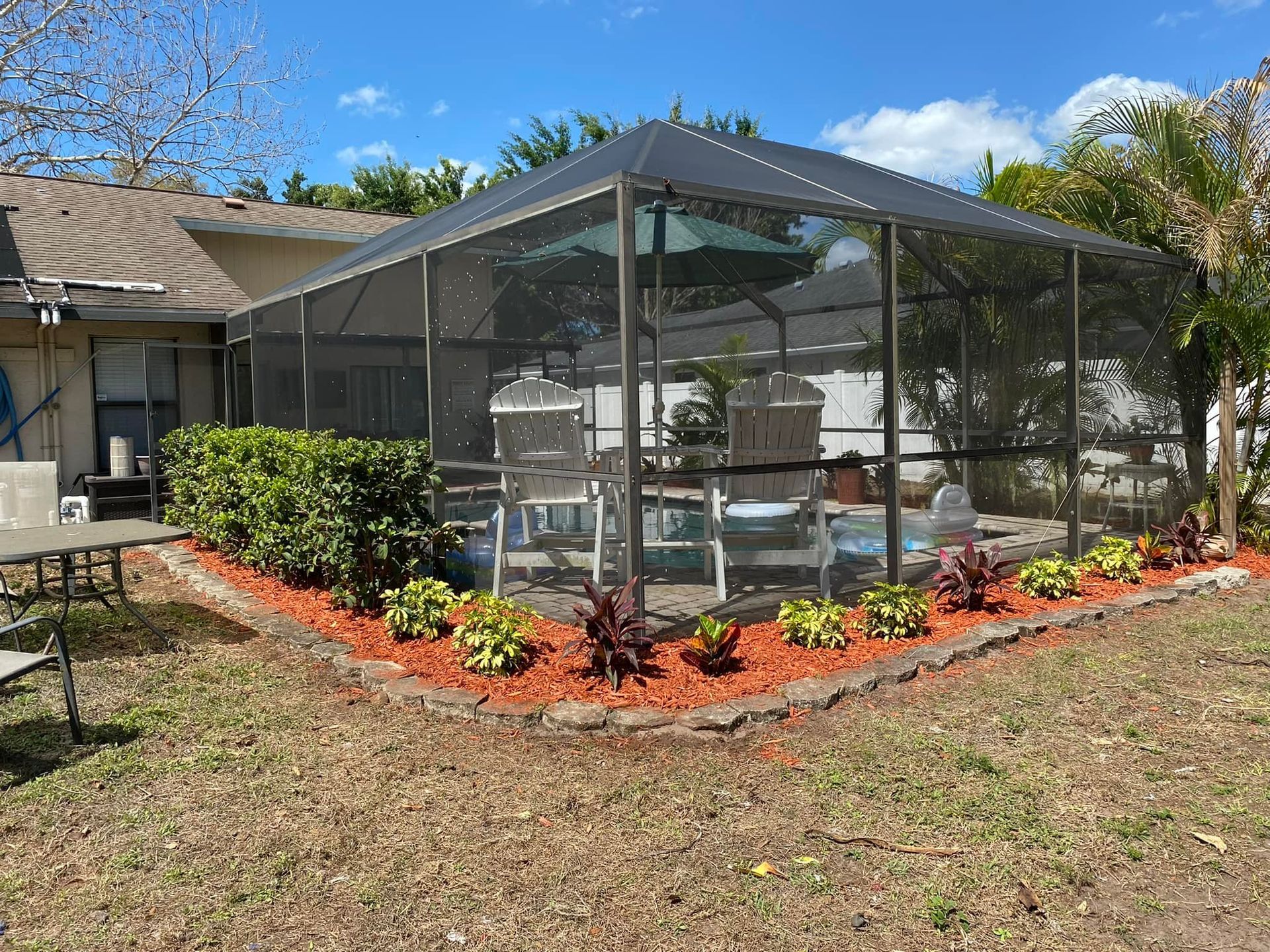 Screened pool enclosure with pool, landscaping, and furniture in a backyard.