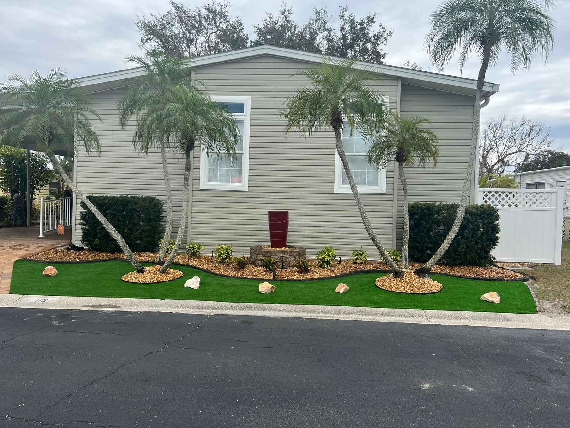 A light gray manufactured home with palm trees and a manicured lawn.