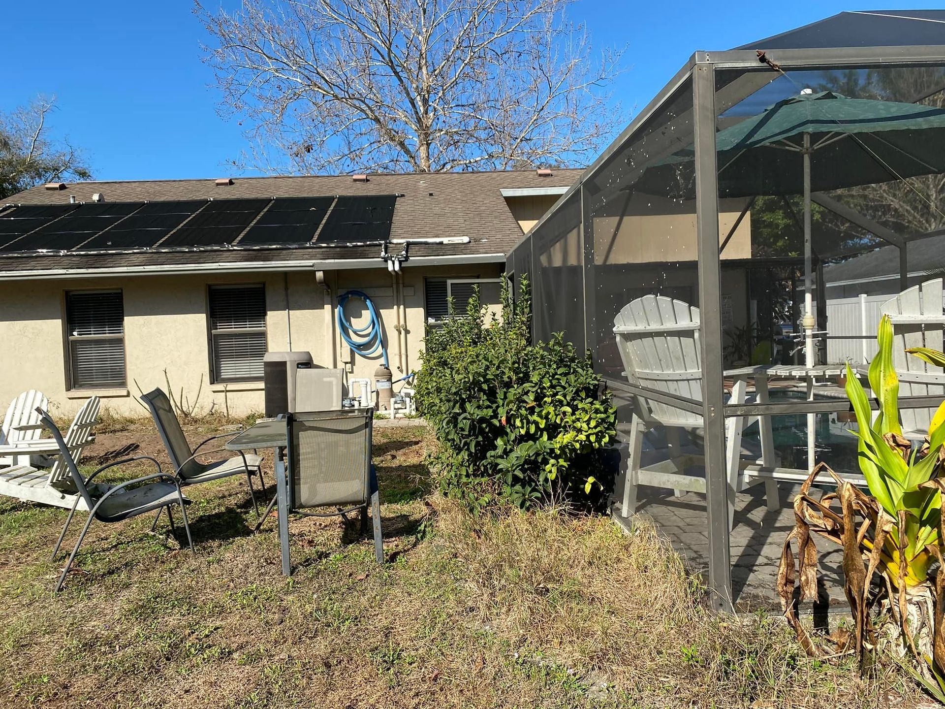 Backyard view: house with solar panels, screened patio with furniture, and lawn with various chairs.