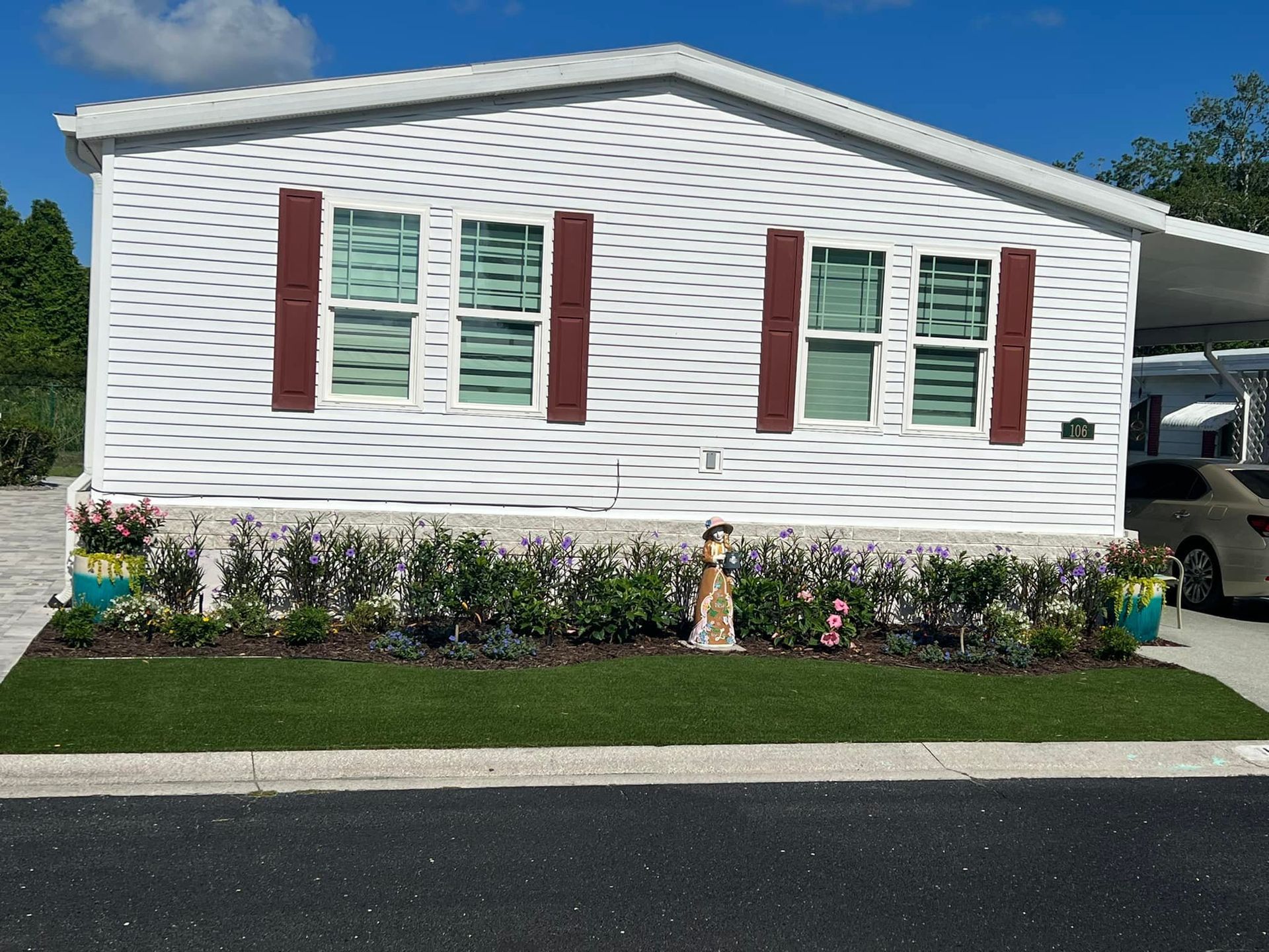 White mobile home with red shutters, manicured lawn, and flower bed.