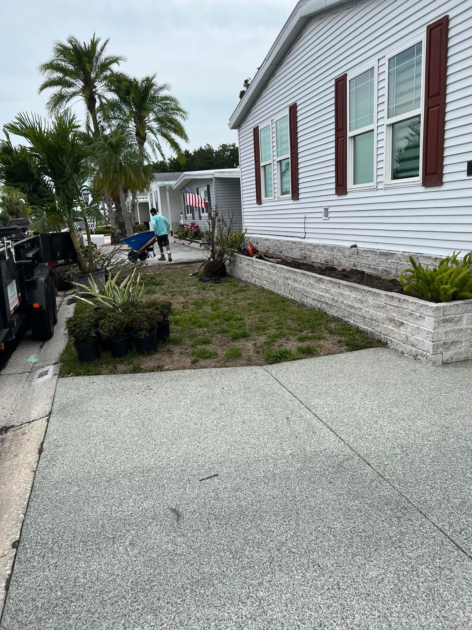 Mobile home with decorative stone landscaping. Person with wheelbarrow near palm trees.