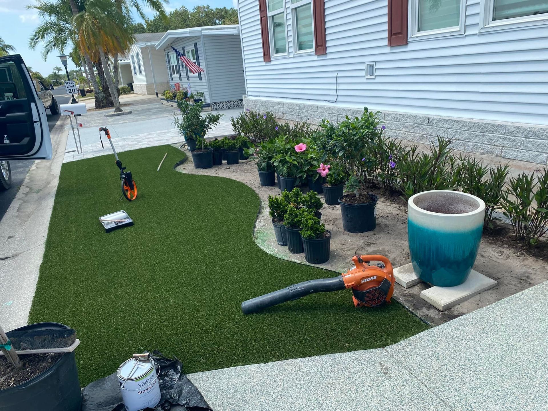 A yard with new green turf, plants in pots, a blower, and a large blue and white pot.