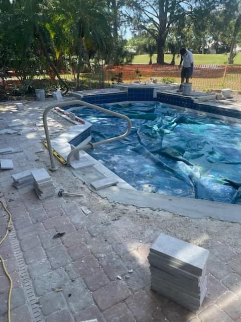 Pool construction: Tiled border around a pool with blue water. A worker applies tiles.