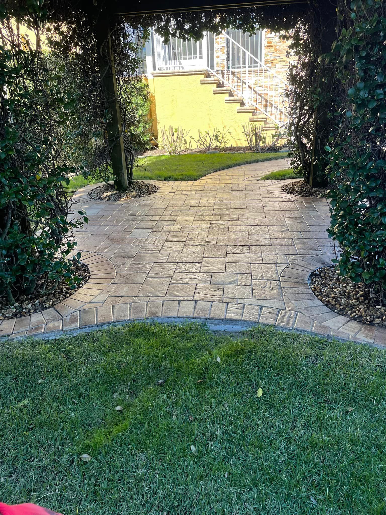 Stone pathway through green garden, leading to yellow house with stairs.