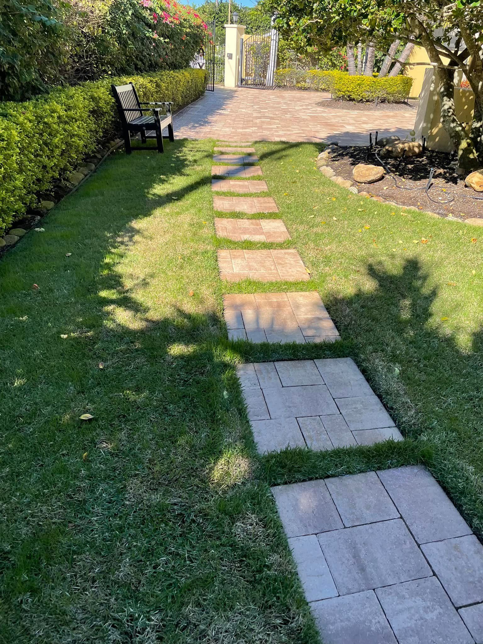 Stone path through grassy yard, hedge on left, bench in distance.