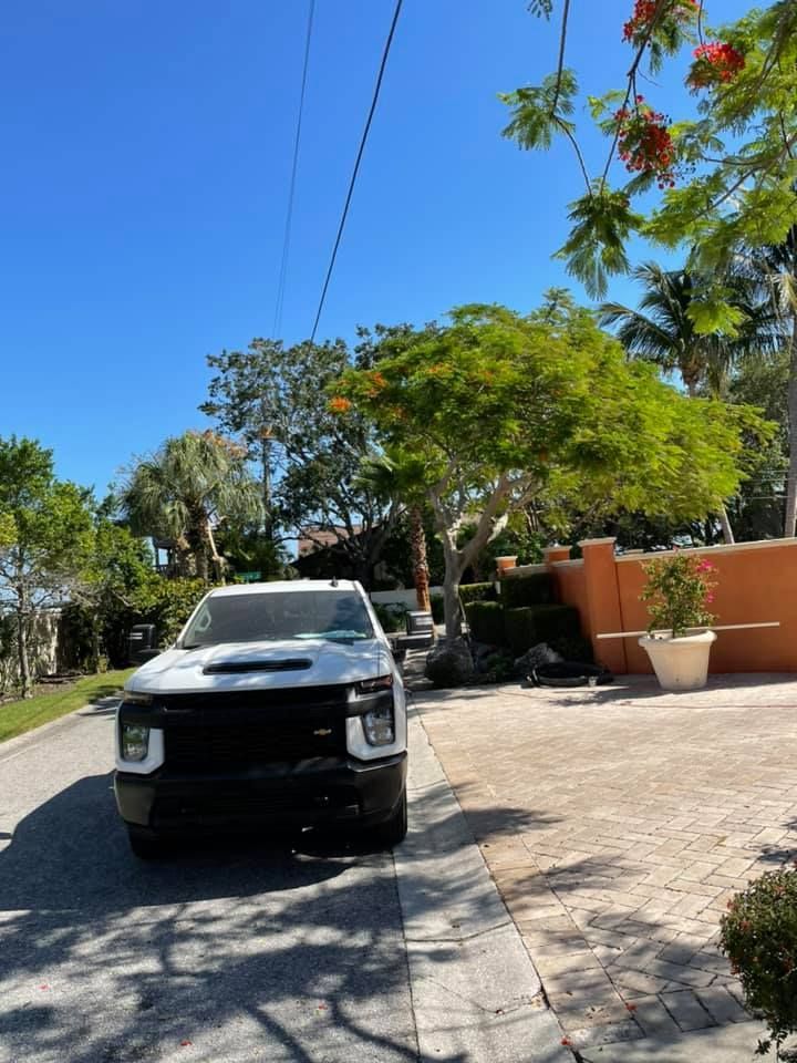 White truck parked on a cobblestone driveway, surrounded by greenery and trees under a clear blue sky.
