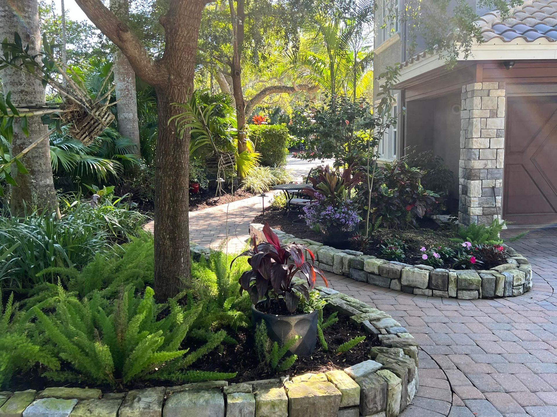 A landscaped garden with a stone-lined flower bed, brick pathway, and a house with a stone facade.