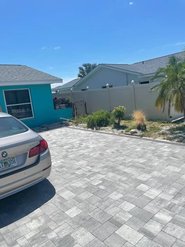 Tan car parked on gray paver driveway; turquoise house on left, fence and other houses in background.