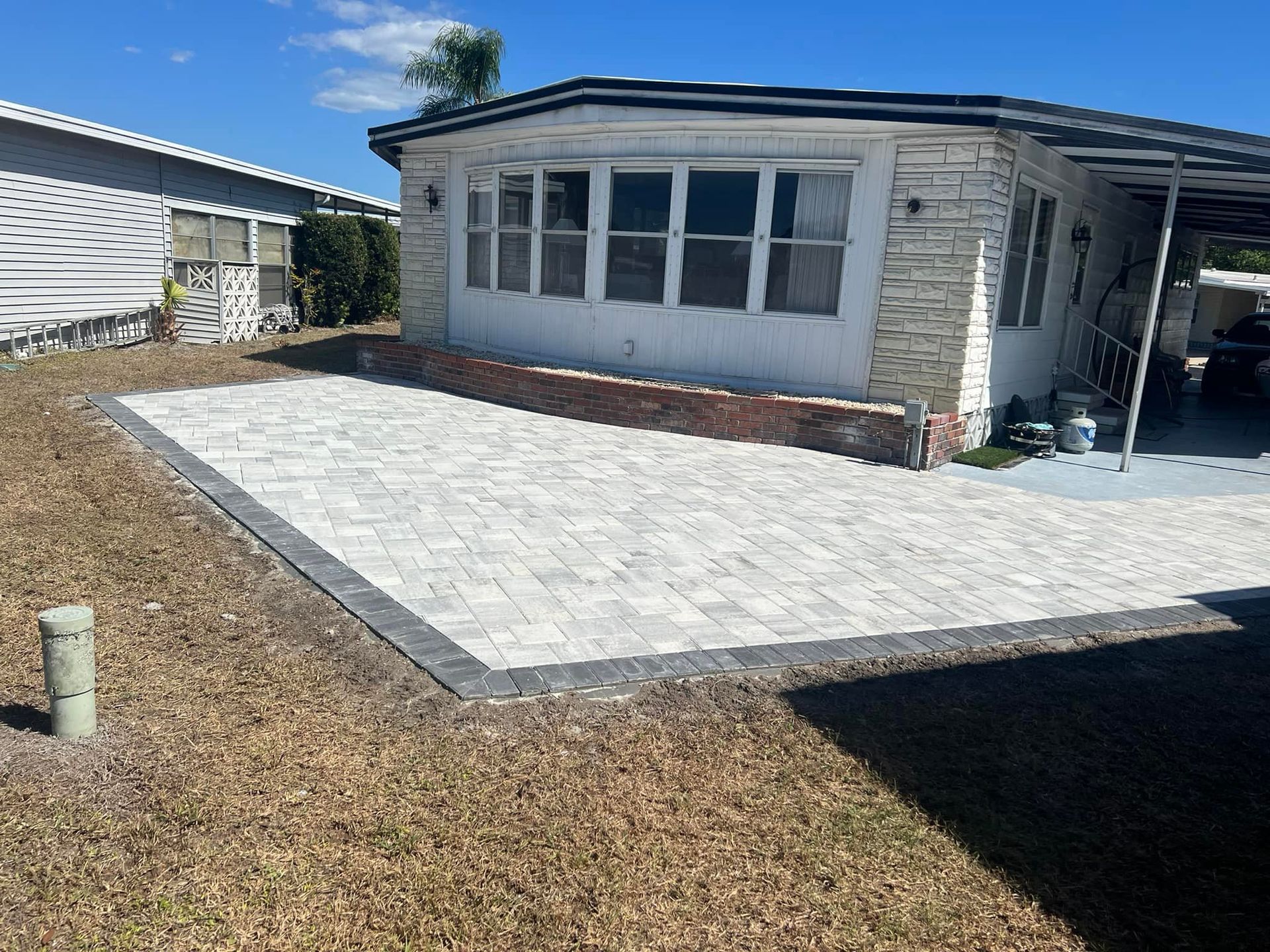 Exterior view of a house with a brick facade and new paved patio in dry grass.