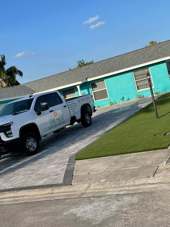 White truck parked on a driveway in front of a turquoise house, with green artificial grass.
