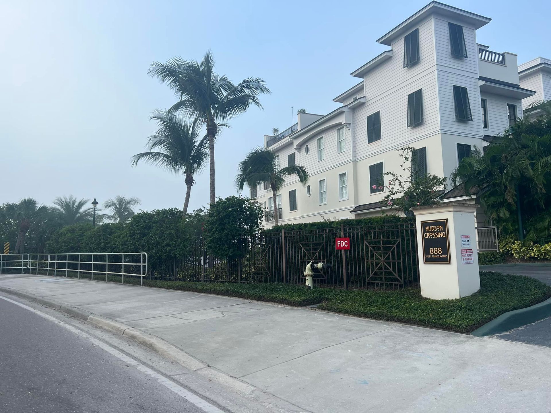 White multi-story building with a tower, palm trees, and a sign.