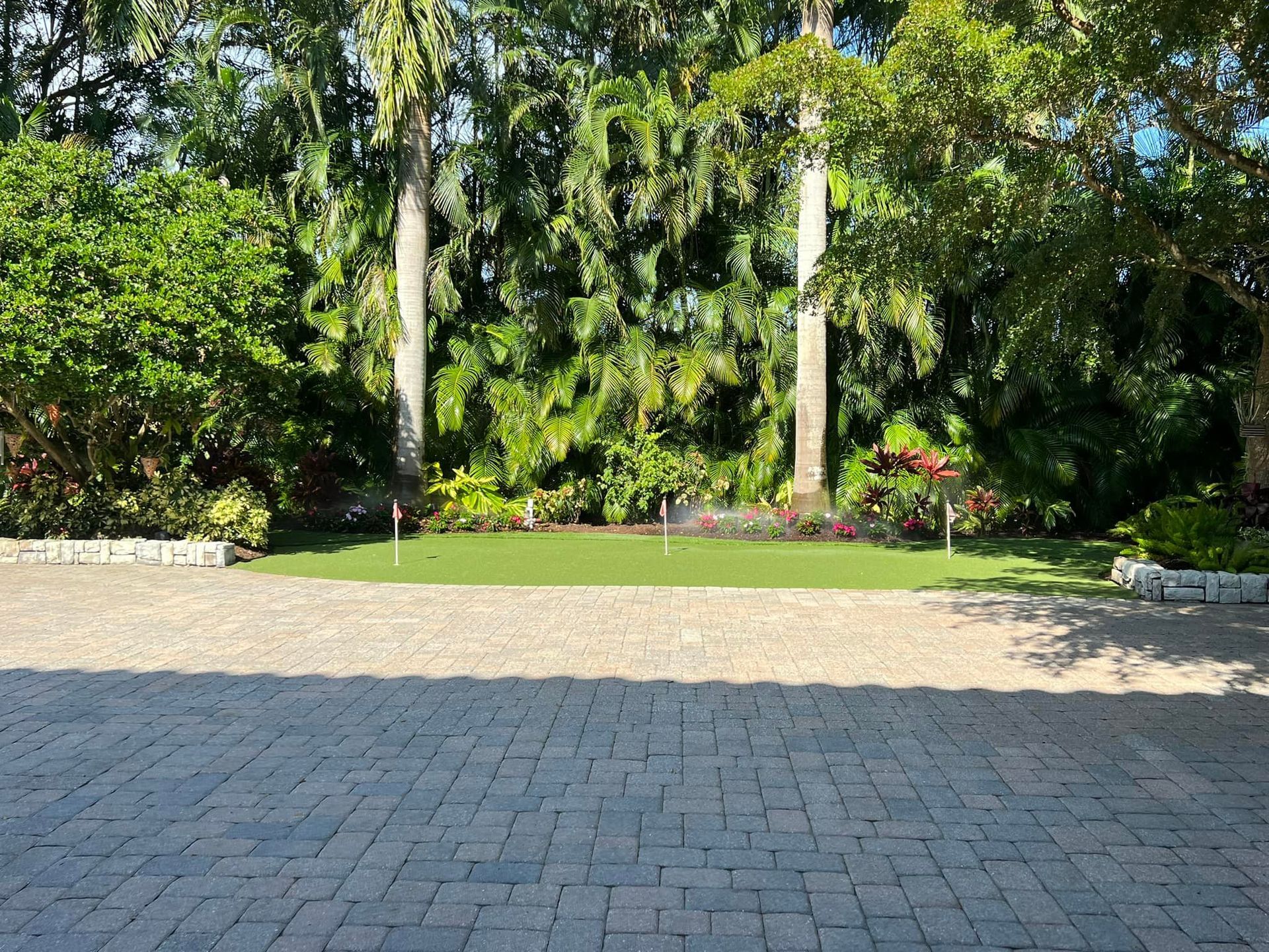 Brick paved area leads to a grassy space surrounded by trees and lush green foliage.