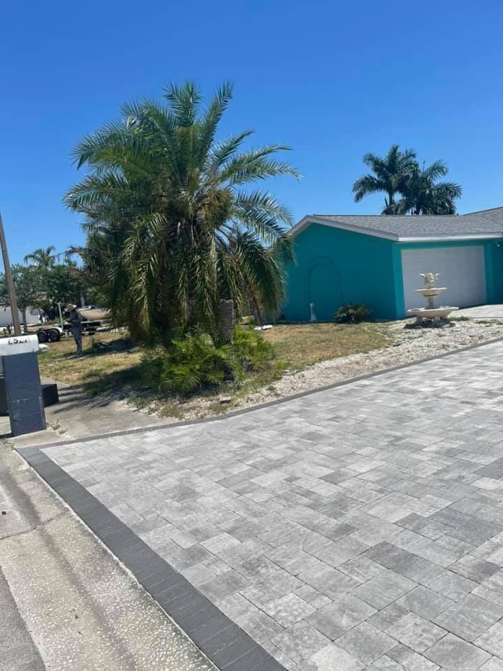 A light blue house with a fountain and palm tree in front, with a paved driveway.