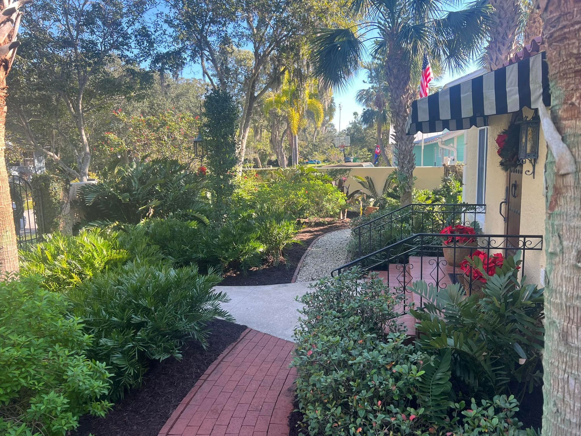 Pathway of red bricks leading to a building with a striped awning, surrounded by lush greenery and trees.