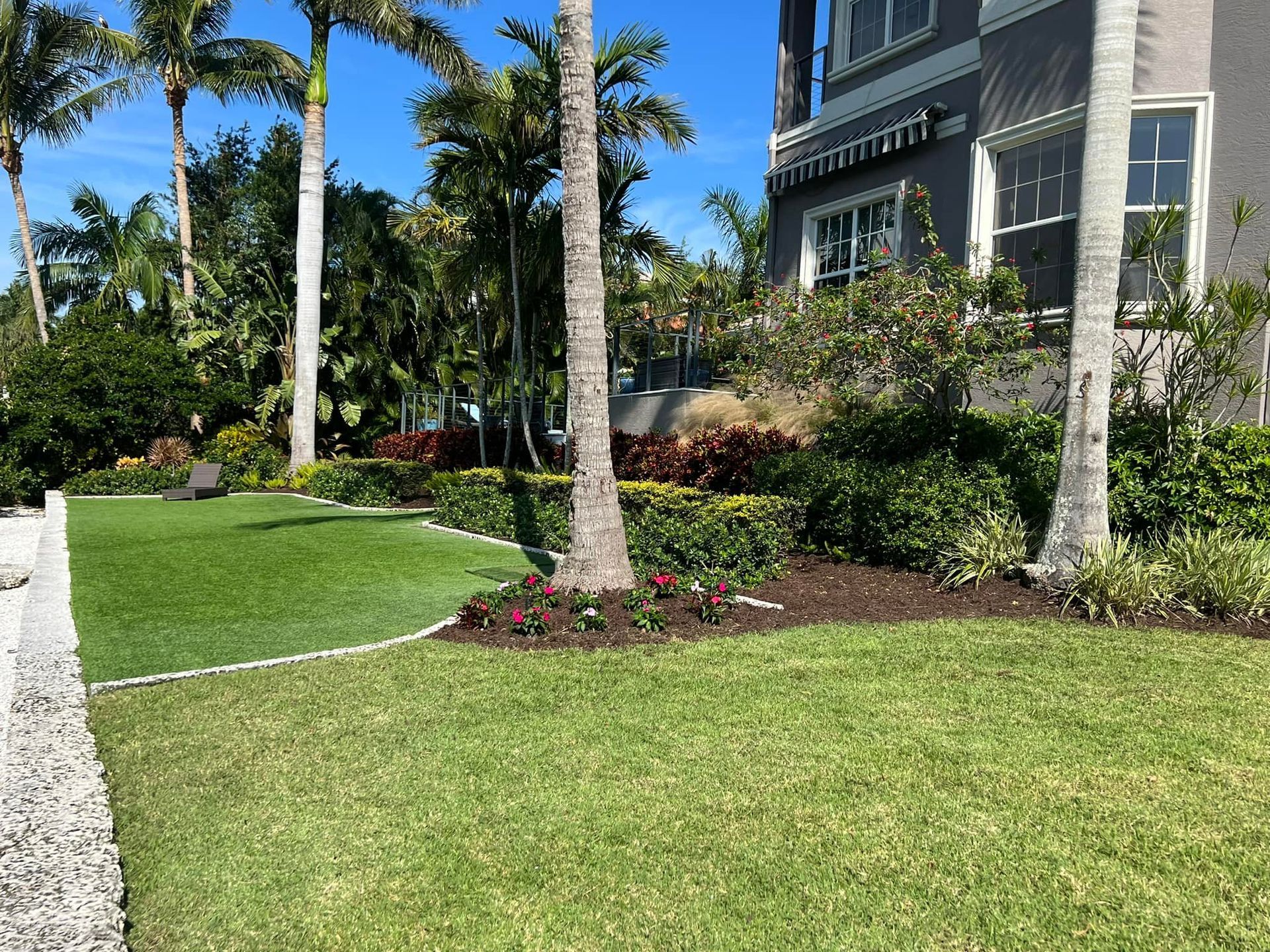 Green lawn and landscaped garden in front of a building with palm trees.