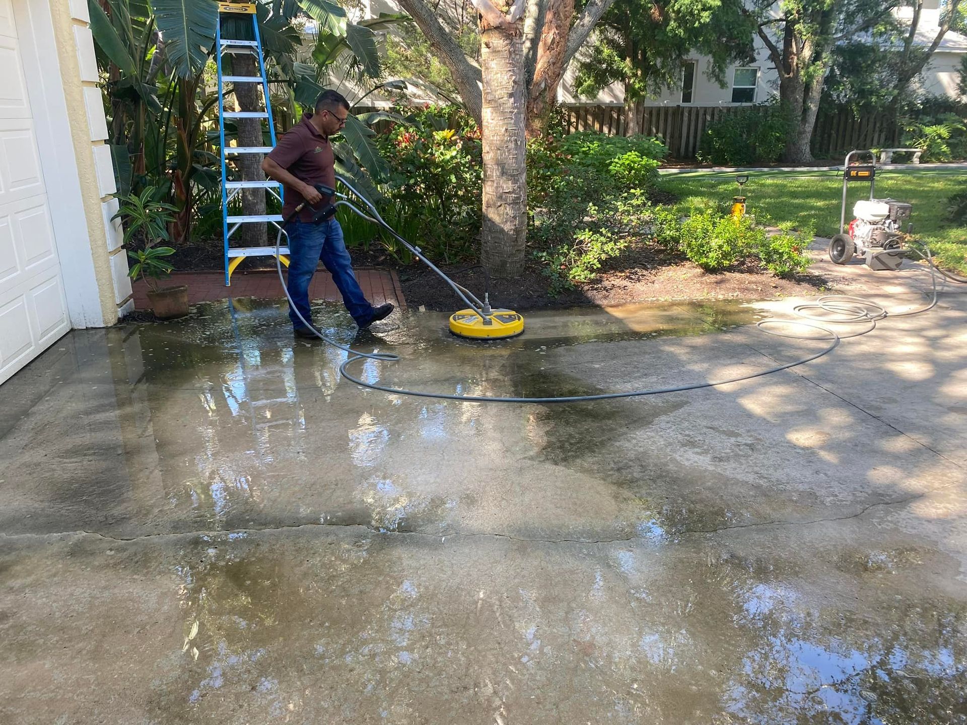 Man pressure washing a concrete driveway with a yellow surface cleaner.