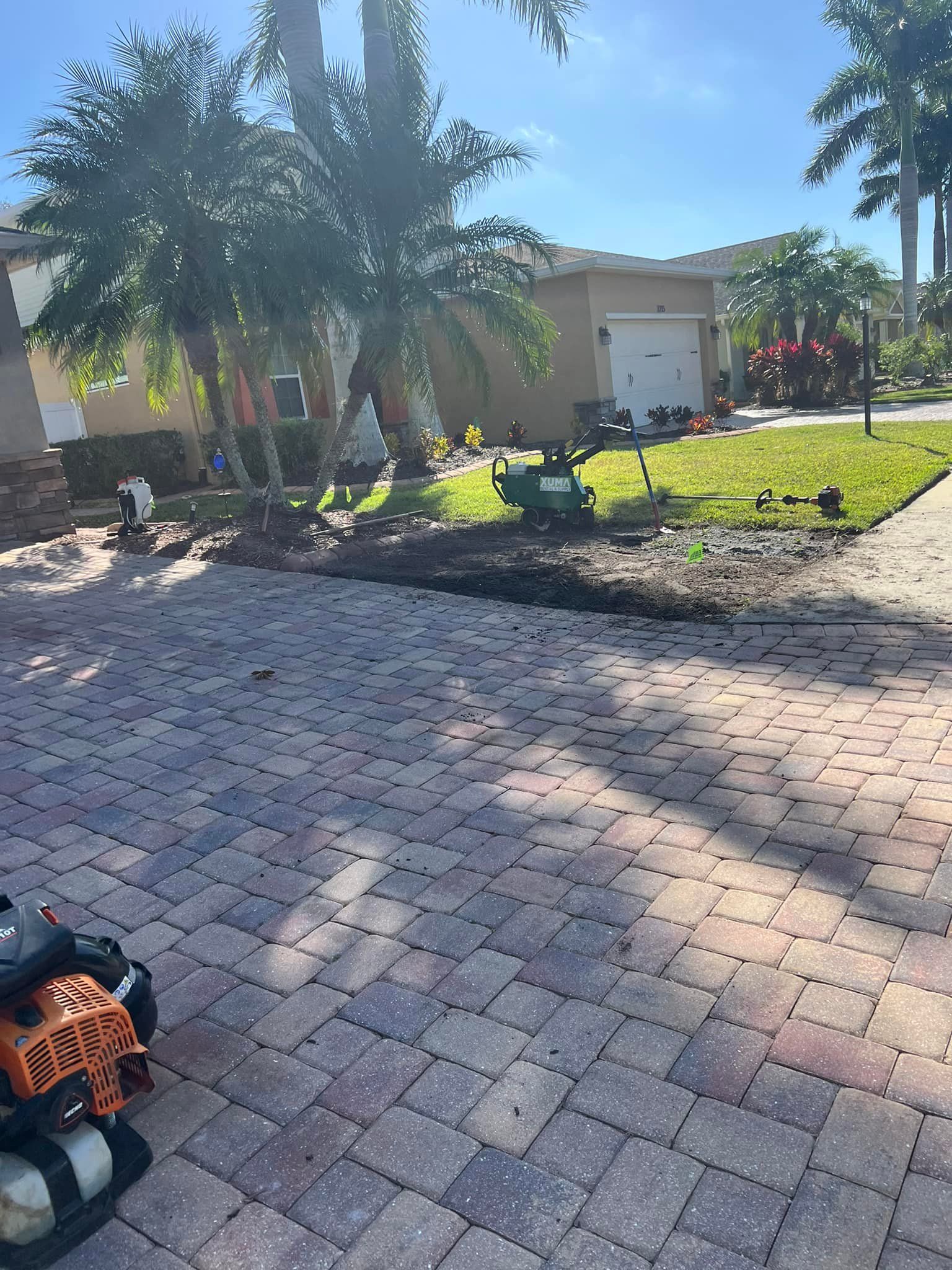 Paver driveway leading to a house with landscaping. A small machine is on the lawn.