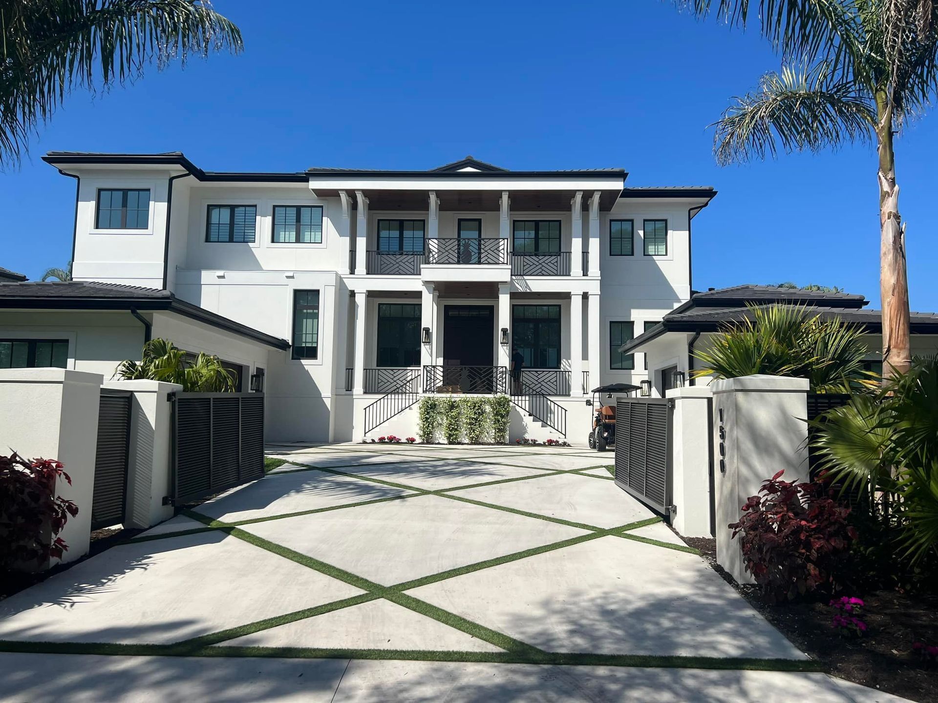 Modern white house with dark trim, gated entrance, and landscaped yard.