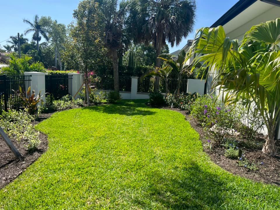 Lush green lawn with manicured edges and surrounding flower beds under a bright blue sky.