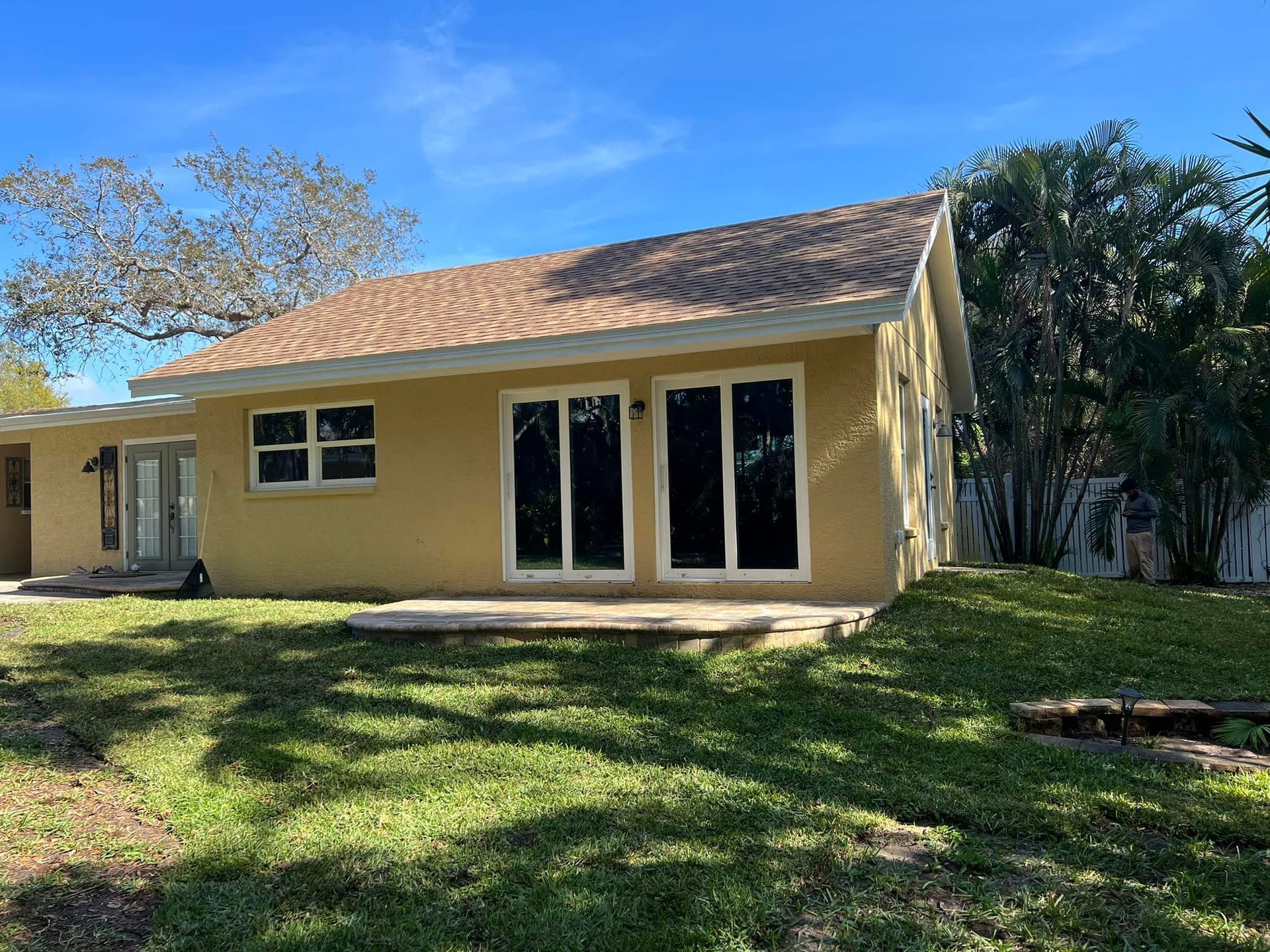 Yellow house with brown roof and large sliding glass doors, on a grassy lawn under a blue sky.