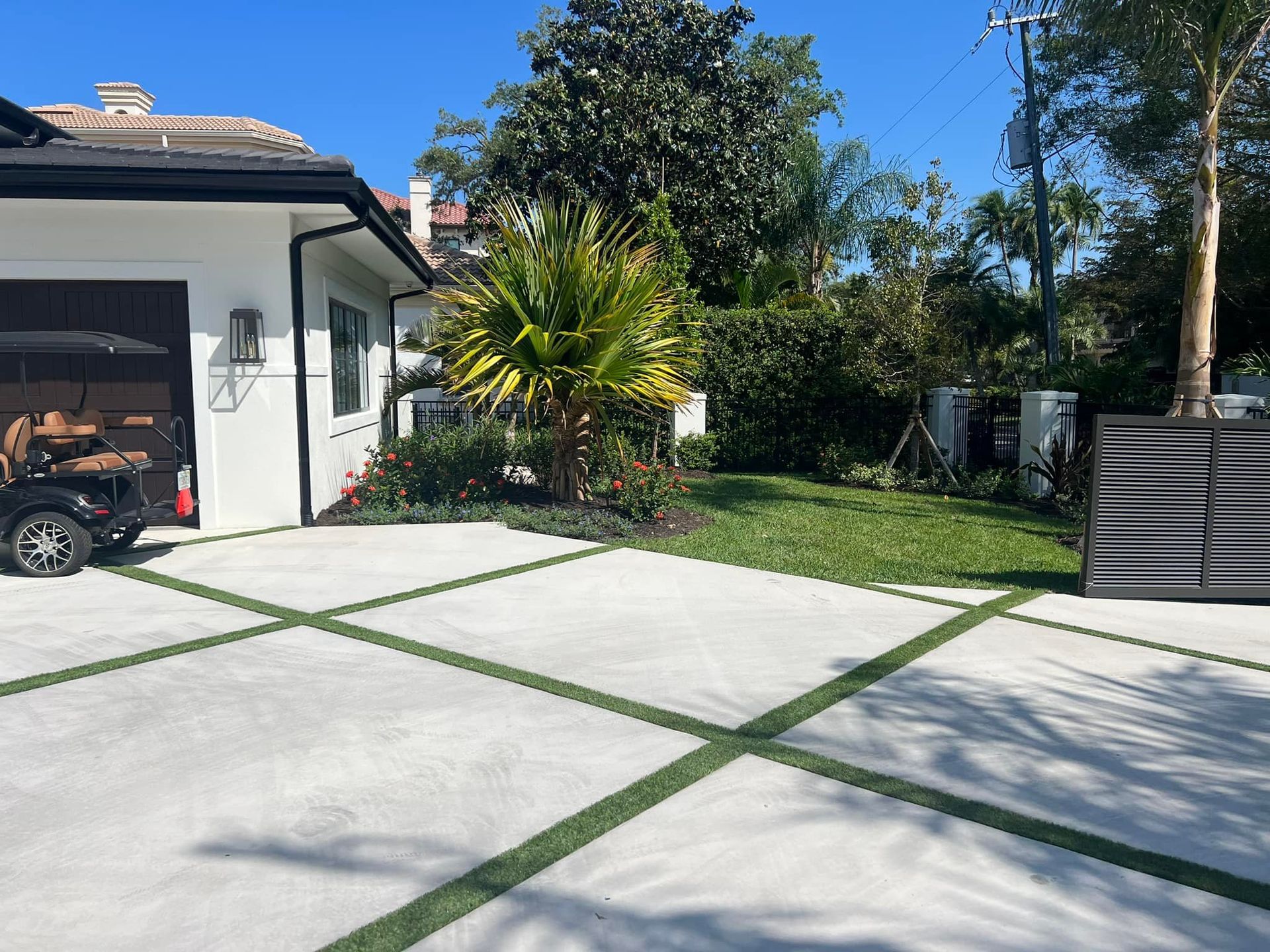 Driveway with green artificial turf grid, white house, palm tree, and black electric scooter.