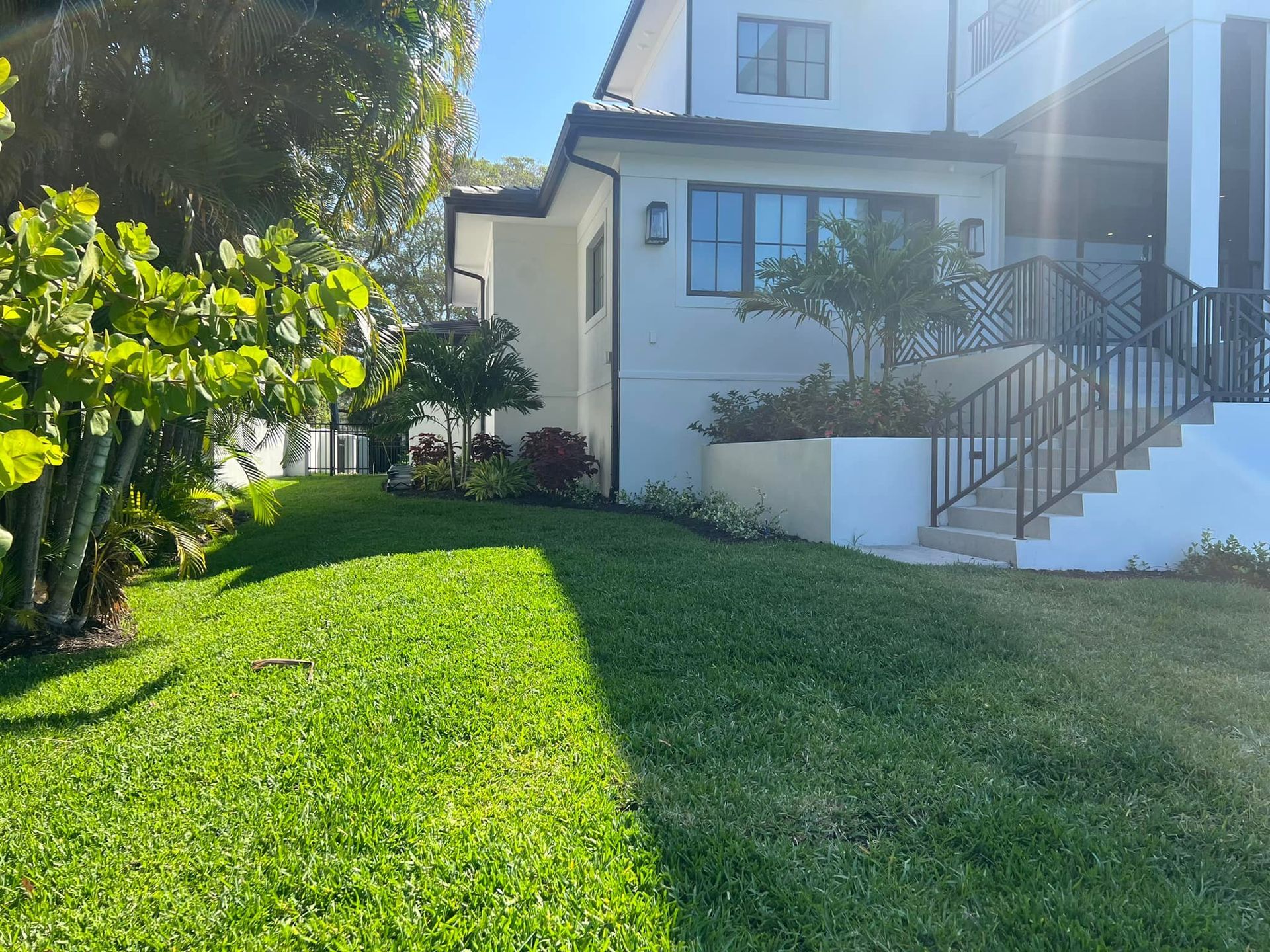 A house with a green lawn, stairs, and a black railing on a sunny day.