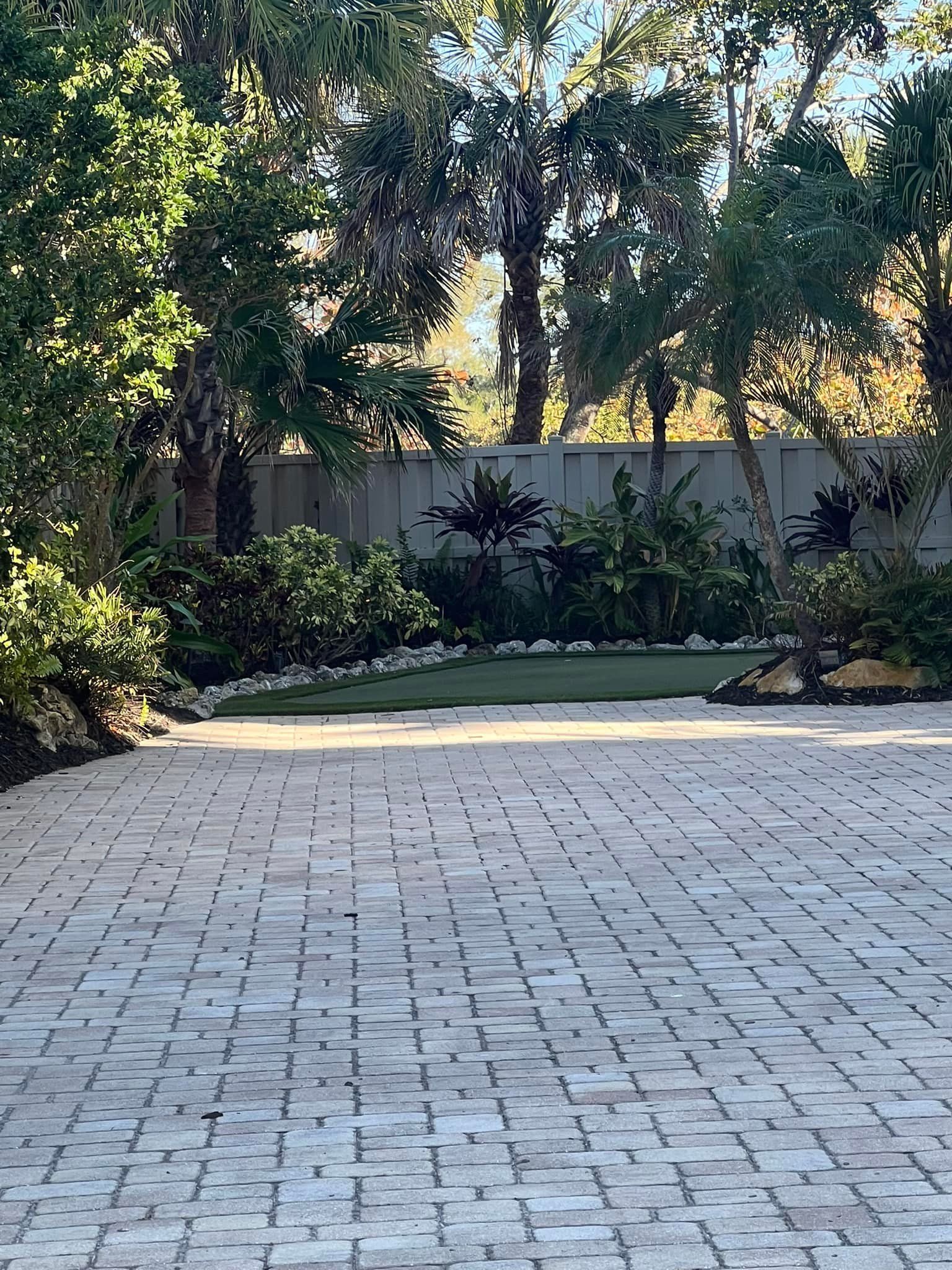 Brick patio with greenery backdrop and trees under a bright sky.