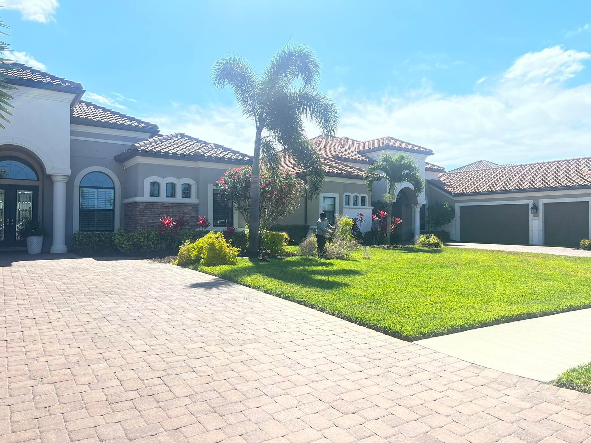 Large house with tiled roof, green lawn, and brick driveway under a sunny sky.
