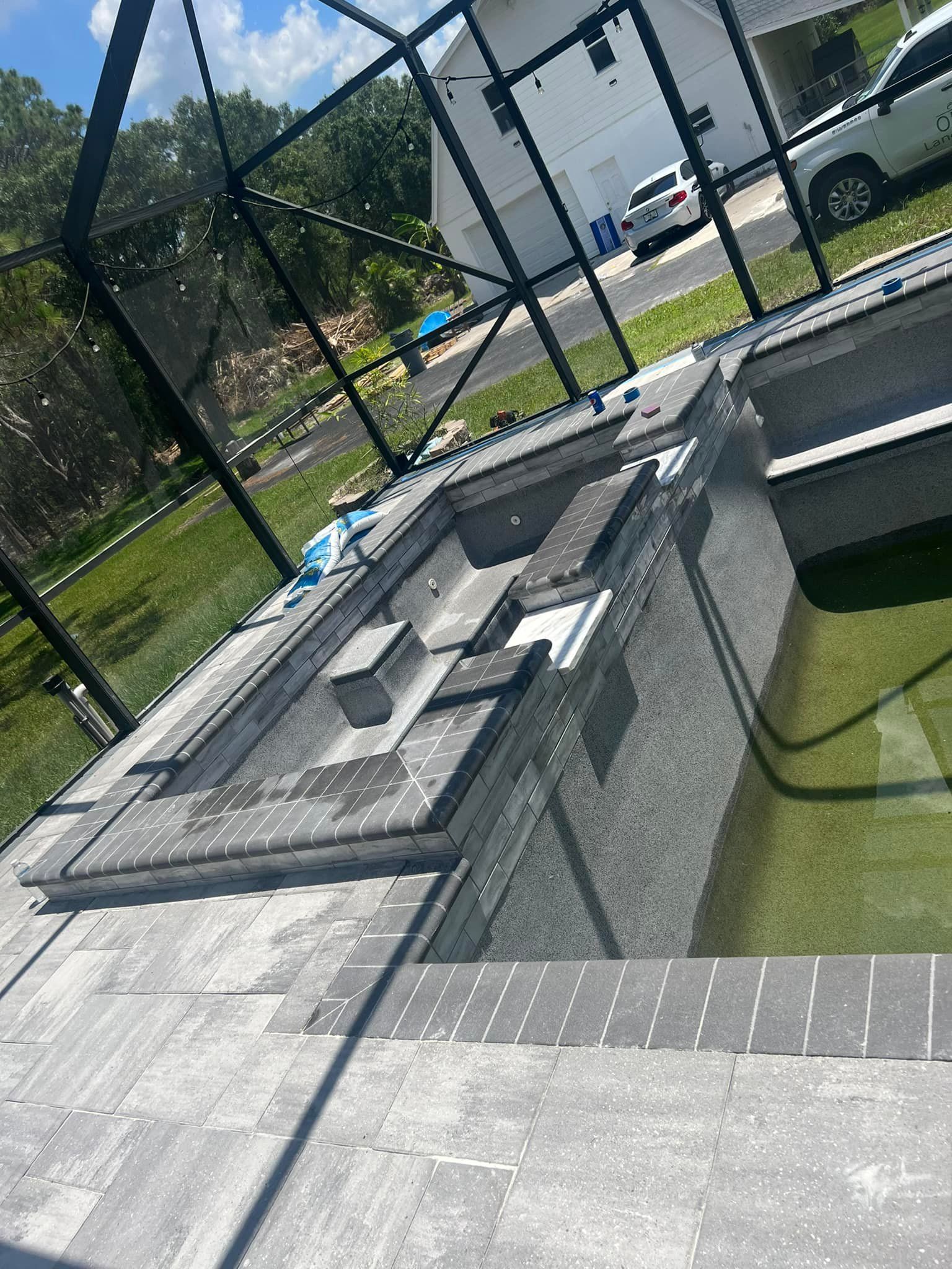 A modern gray swimming pool with a spa, enclosed by a black screen, in a backyard.