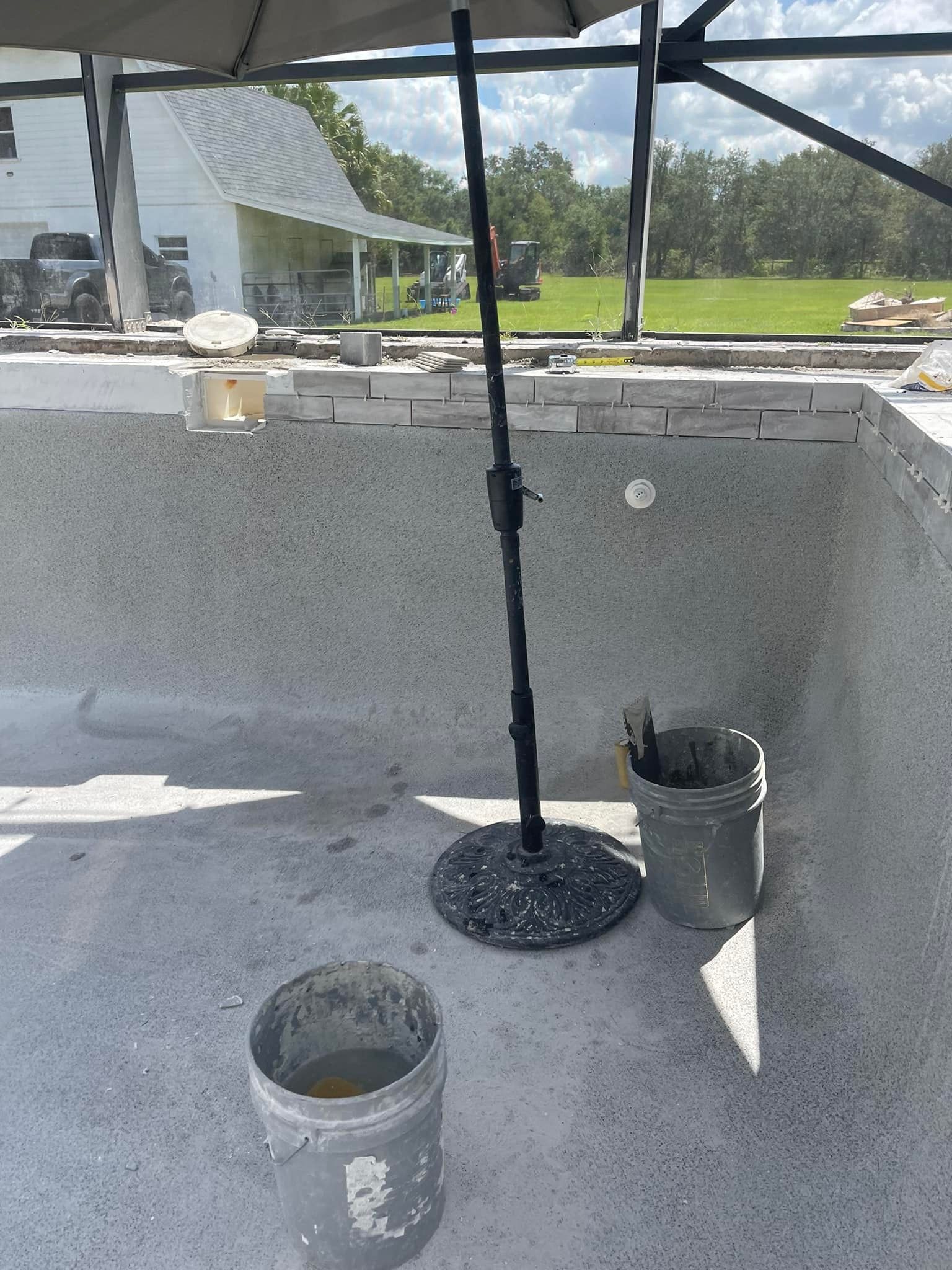 Pool under construction with umbrella, buckets, and gray walls.