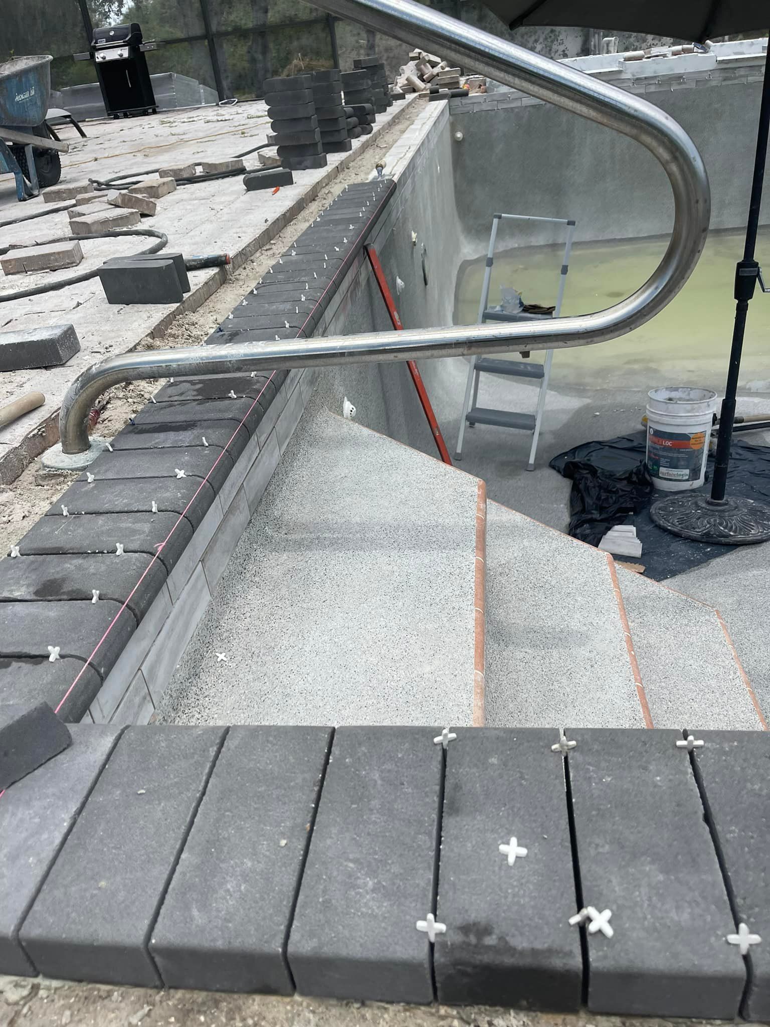 Pool coping and steps under construction with a stainless steel handrail.