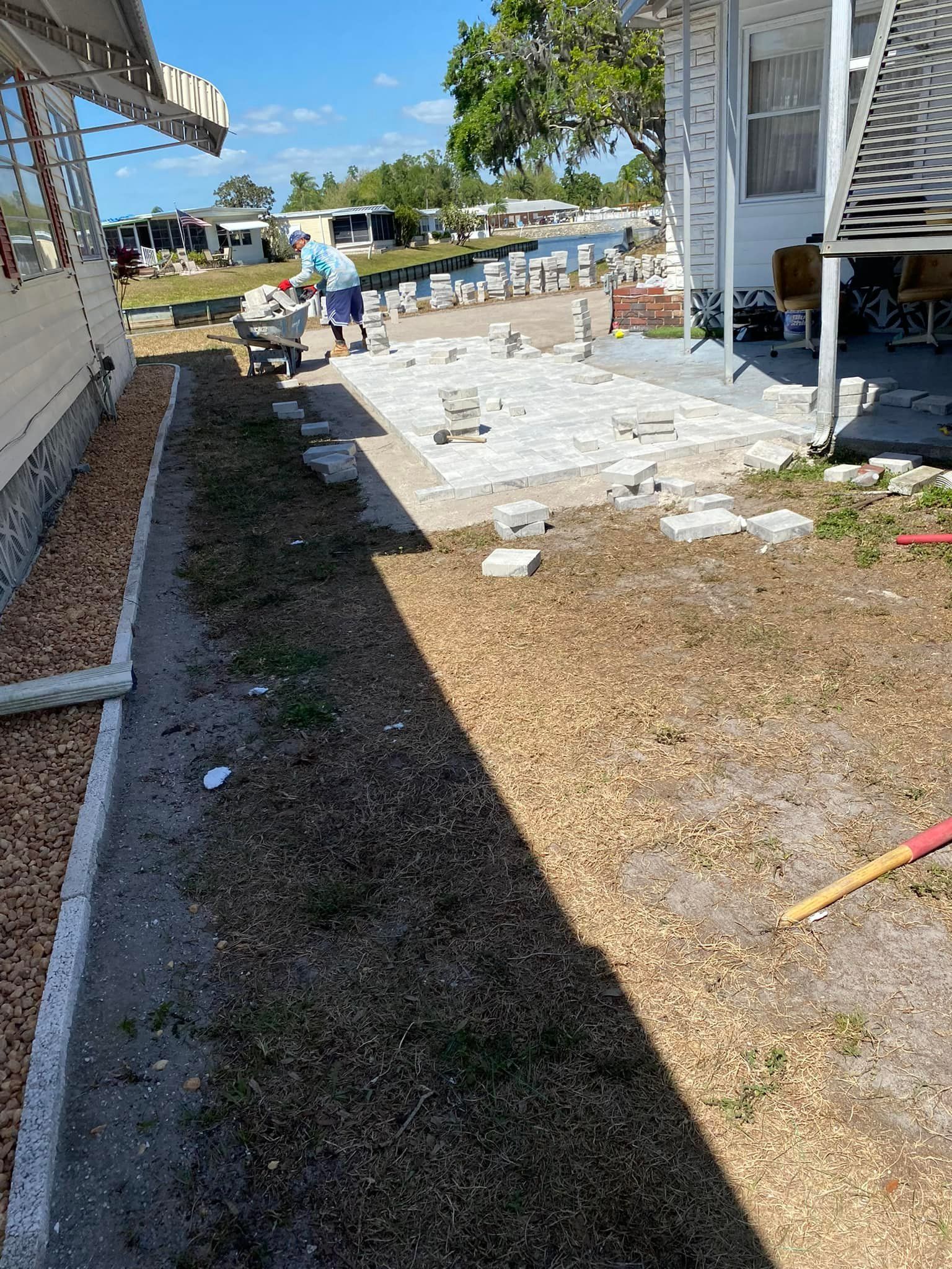 Workers laying pavers on a patio next to a house with gravel and grass.