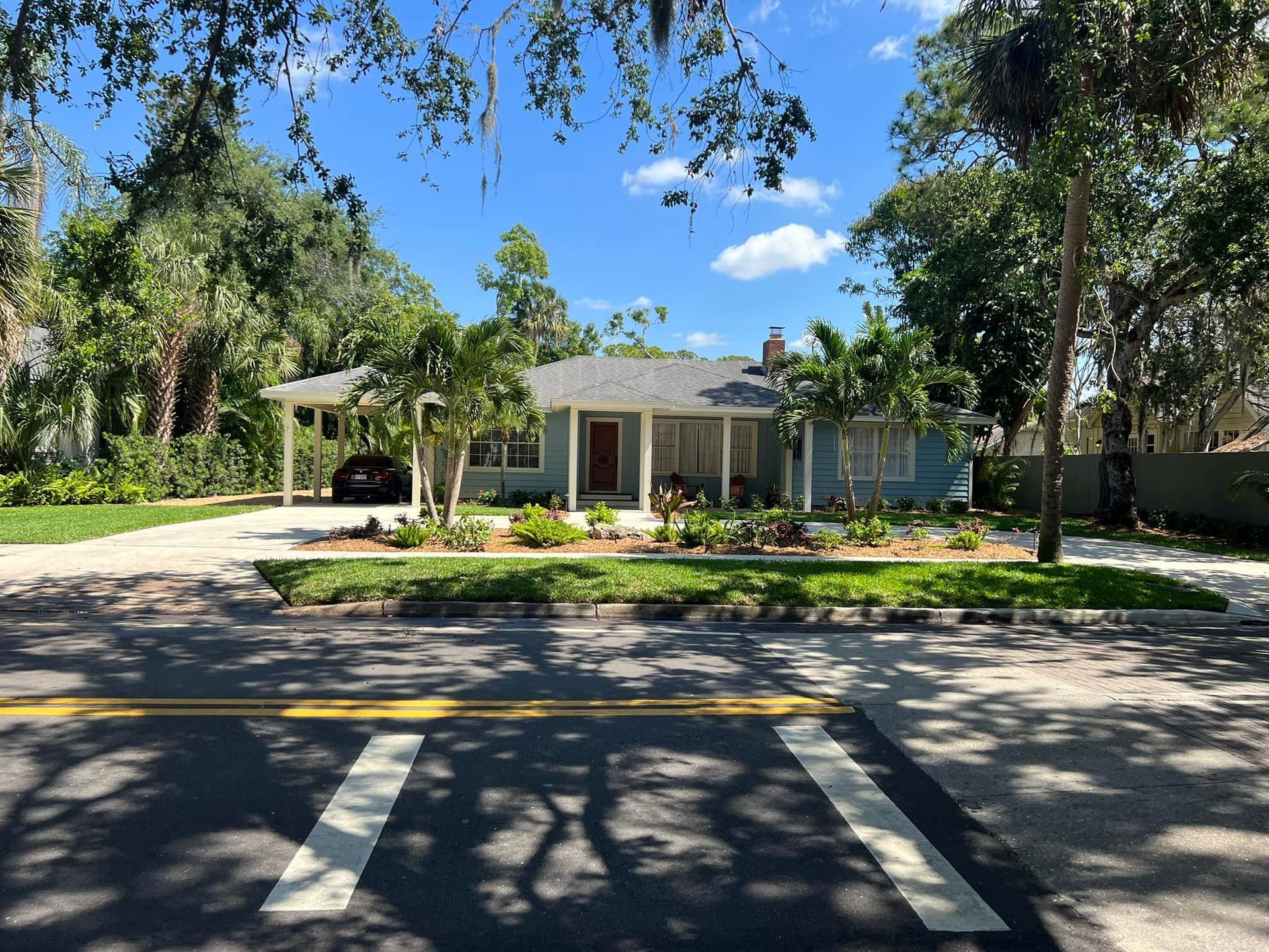 Blue house with white trim, gray roof, and landscaped yard, viewed from across a road.