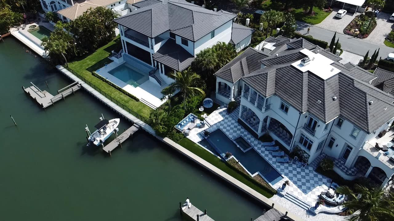 Aerial view of two waterfront mansions with pools and docks.