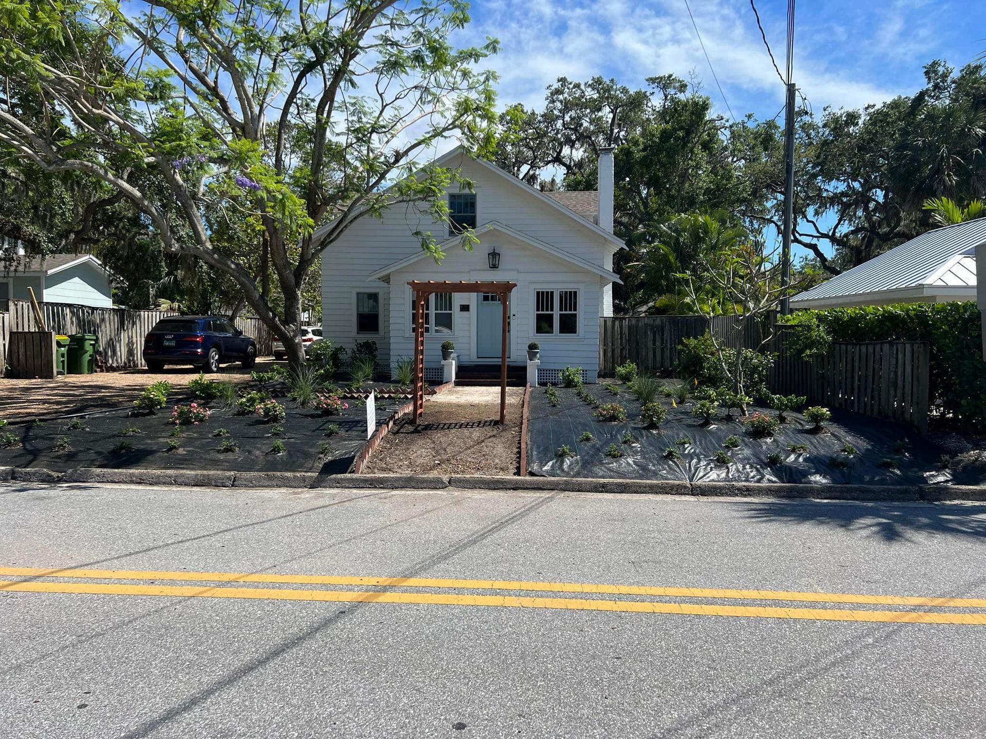 White house with small front yard garden, flanked by fences, set back from a sunny street.