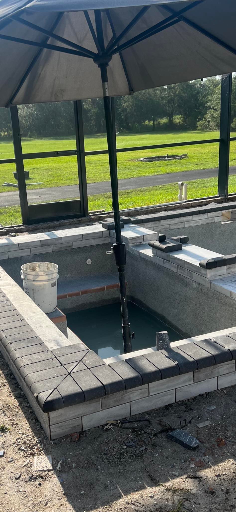 A rectangular brick structure with water inside and an open umbrella overhead.