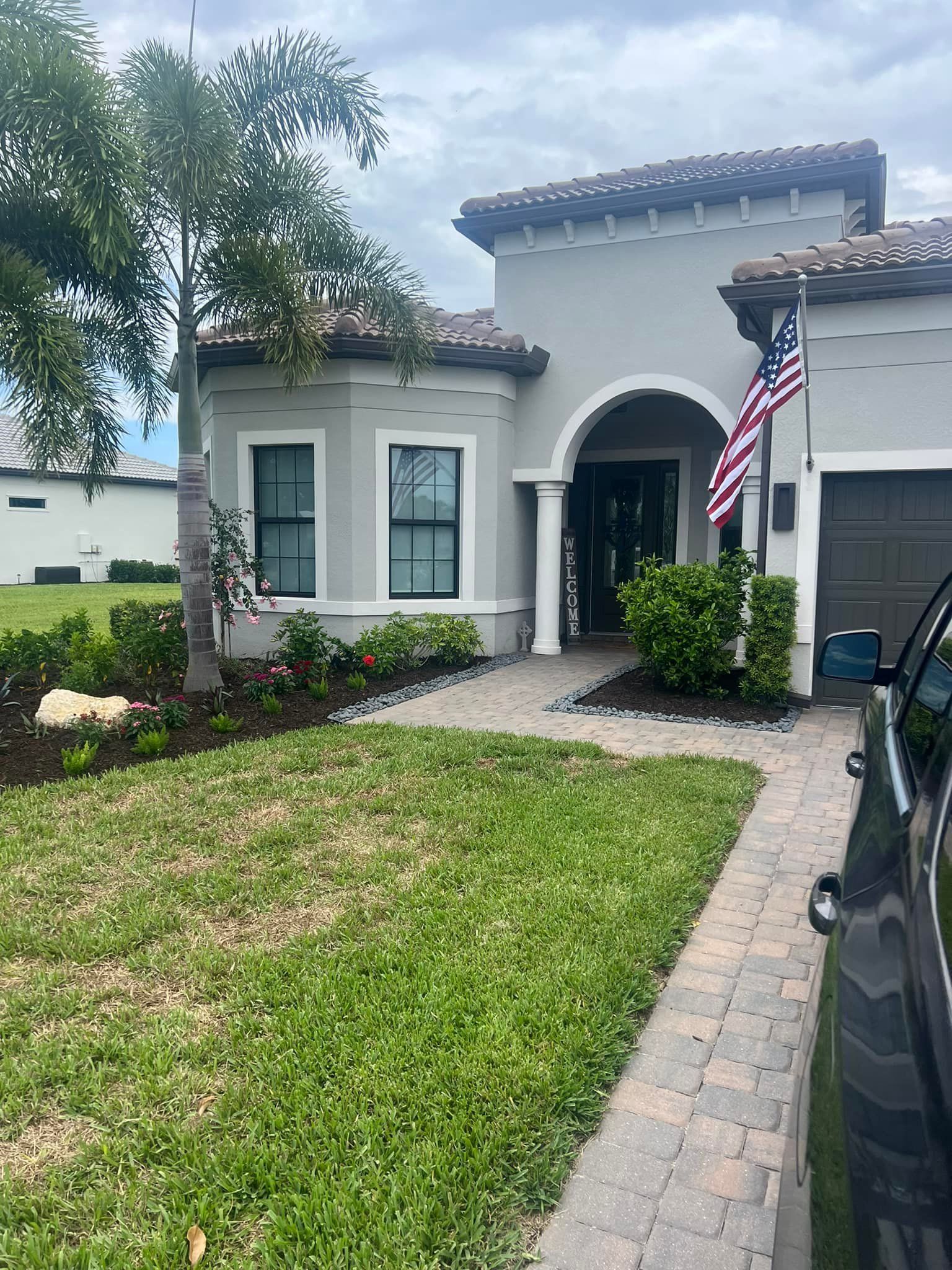 Exterior of a light gray house with a red-brown roof. American flag, palm tree, and black car are present.