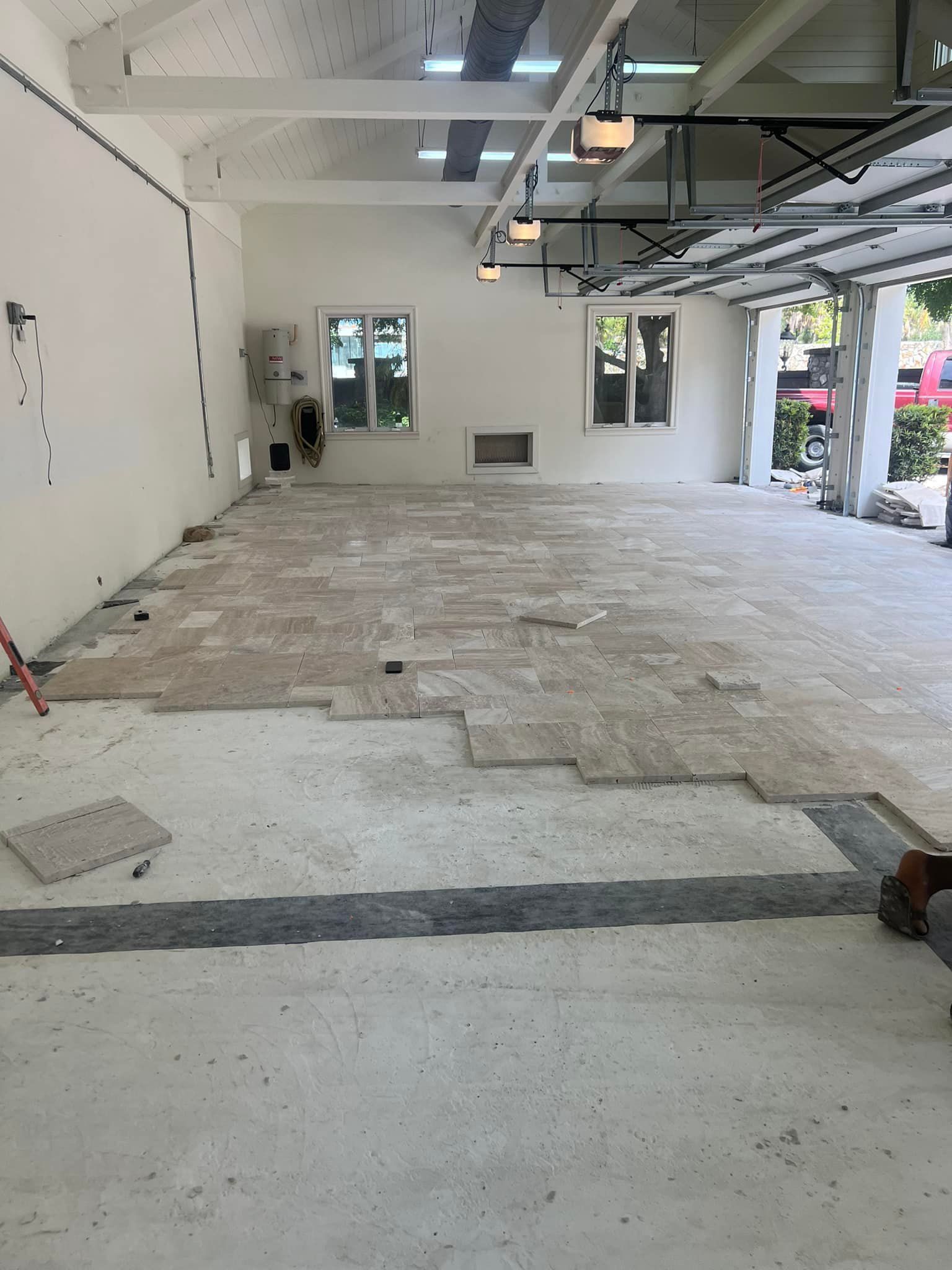 Interior space under construction; stone tiles partially installed on a concrete floor. Windows on white walls.