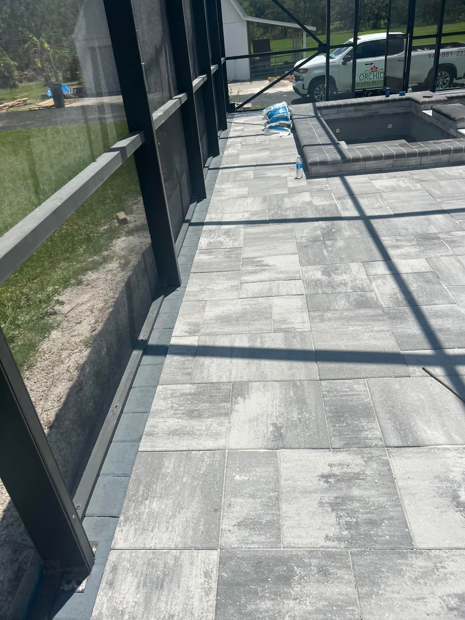 Grey paver patio next to a black screen enclosure and a small pool.