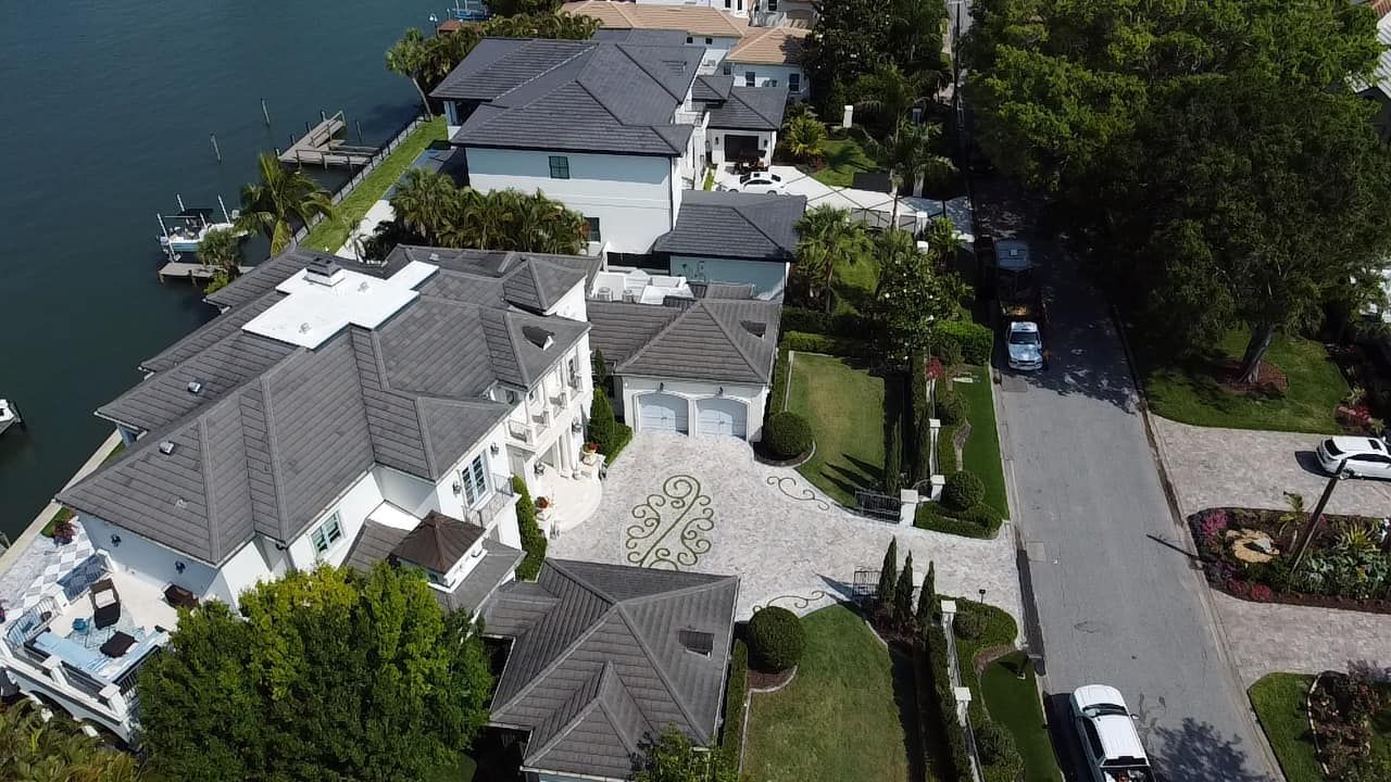 Aerial view of waterfront houses with boats docked, lush landscaping, and a street.