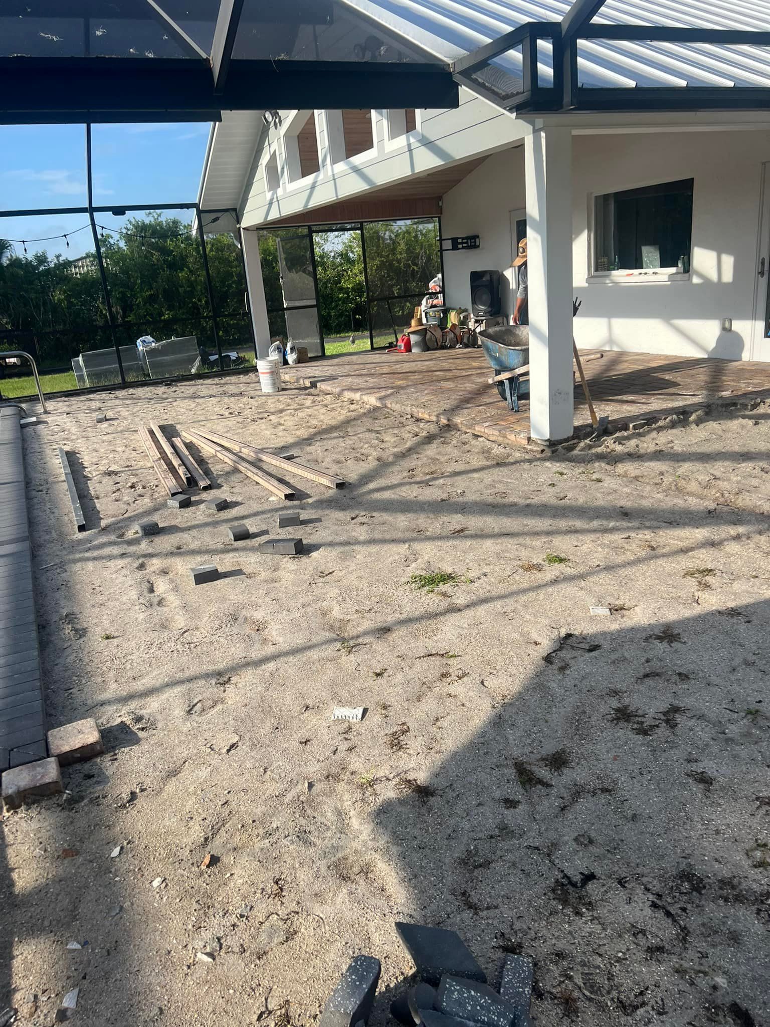 Construction site: Gravel base with bricks laid, next to a white house with a patio roof.